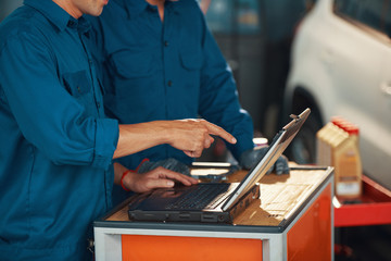 Cropped image of mechanic pointing at laptop screen and discussing results of car computer diagnostics with coworker