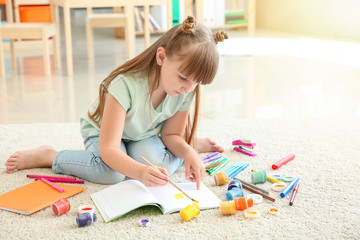 Cute little girl painting while sitting on carpet