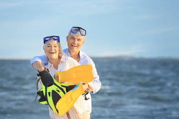 Happy mature couple with snorkeling masks and paddles having fun at sea resort
