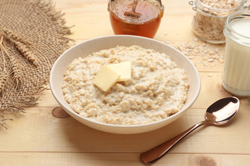 Bowl with tasty oatmeal, milk and honey on wooden table