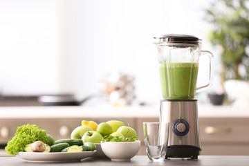 Blender with tasty smoothie and ingredients on table in kitchen