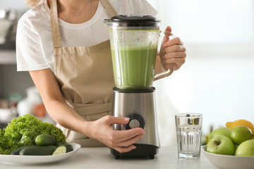 Woman preparing tasty green smoothie in kitchen