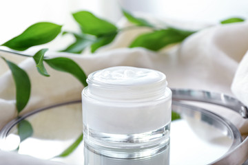 Jar of body cream with herbal extract on table