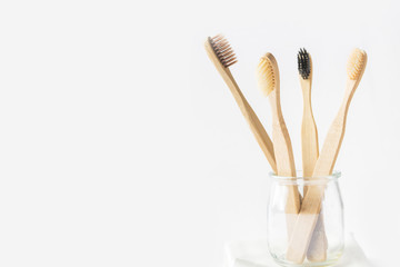 Charcoal wooden bamboo toothbrushes in glass cup on white background. Zero waste plastic free eco...