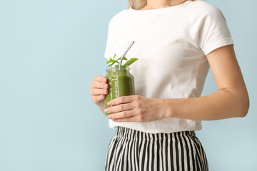 Young woman with tasty smoothie in mason jar on color background, closeup