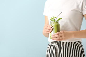 Young woman with tasty smoothie in mason jar on color background, closeup