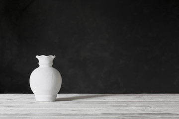white vase on wooden table on black background