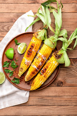 Plate with tasty grilled corn cobs on table
