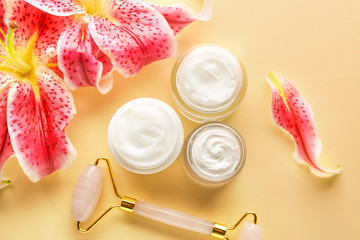 Natural cream with massage tool and flowers on color background