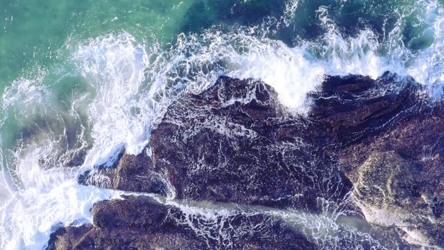 White fringed waves crashing in from top of screen onto sea rocks Tamarama Beach Sydney Australia POV drone directly above