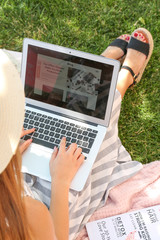 Female blogger with laptop sitting on grass in park