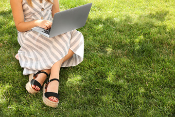 Female blogger with laptop sitting on grass in park