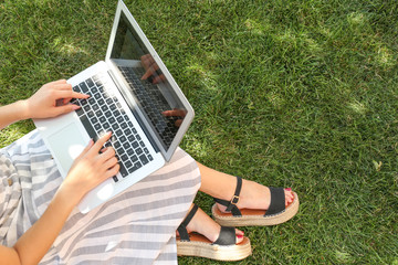Female blogger with laptop sitting on grass in park