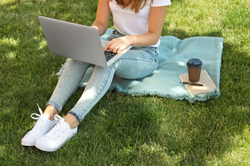Female blogger with laptop sitting on grass in park