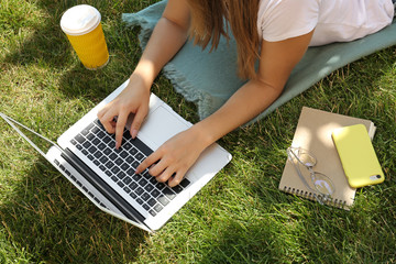 Female blogger with laptop lying on grass in park