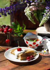 Pancakes with berries. Tasty breakfast with pancakes, cherry and sour cream on rustic wooden table background. Toned image, soft morning light