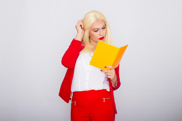 Attractive blonde haired woman wearing red jacket and pants, holding book in her hands