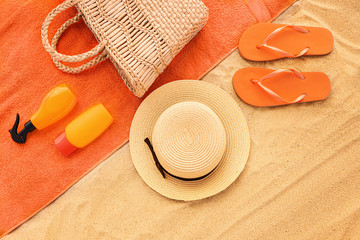 Flip-flops with bag, towel, hat and cosmetics on sand beach