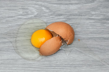 Broken brown egg on a gray wooden table.
