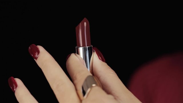 Closeup of red lipstick in golden tube in female hands. In the studio on black background. Opens red lipstick.