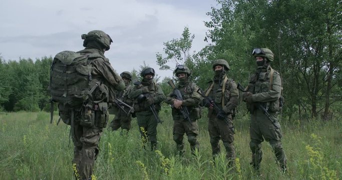 Soldiers in camouflage with assault rifles in field, commander instructs the soldiers, military action in the steppe area.