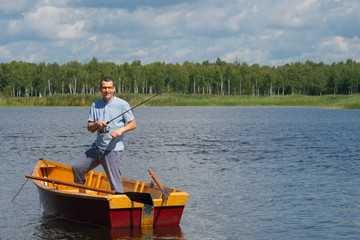 a cheerful man in yellow glasses, in a boat with oars, in the center of the lake, holds a fishing...