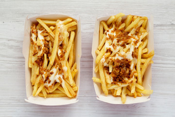 Top view, french fries with cheese sauce and fried onion in a paper box on a white wooden background. Flat lay, from above, overhead.