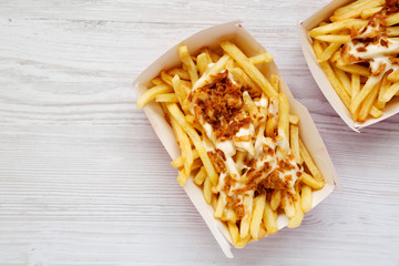 French fries with cheese sauce and fried onion in paper boxes on a white wooden background, overhead view. Flat lay, from above, top view. Copy space.