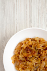 Overhead view, homemade caramelized onions on a white plate on a white wooden table. Flat lay, overhead, from above. Copy space.