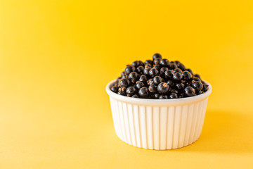 Ripe black currant or blueberries in a small white Cup on a yellow background. Black currant harvest. Healthy food. vegetarian food