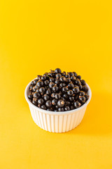 Fototapeta na wymiar Ripe black currant or blueberries in a small white Cup on a yellow background. Black currant harvest. Healthy food. vegetarian food