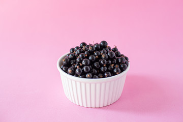 Ripe black currant or blueberries in a small white Cup on a pink background. Black currant harvest. Healthy food. vegetarian food.