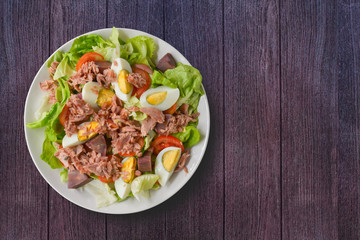 Top view. Tuna salad with lettuce, tomato sliced, boiled egg and sweet potato in white bowl on dark wooden table background. Healthy food to high fiber, vitamins and low carbohydrate, fat, copy space.