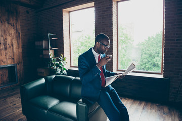 Dark skin macho guy leaning office sofa drinking hot beverage reading fresh press wear elegant...