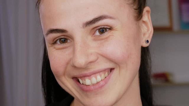 Portrait of a smiling girl with freckles without makeup, looks in the frame. Brown-eyed brunette with a clean face before applying makeup