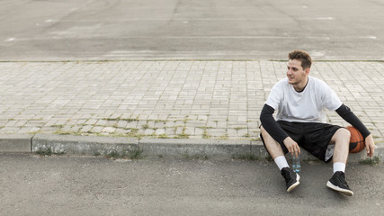 Front view man sitting with a basketball