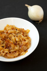 Homemade caramelized onions on a white plate on a black background, low angle view. Close-up.