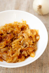 Homemade caramelized onions on a white plate, side view. Close-up.