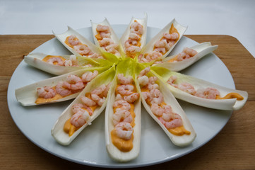 Shrimp appetizer with sauce in lettuce leaves on white plate. Wooden table, white background 