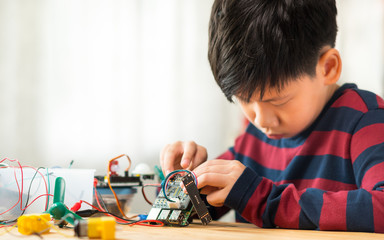 Smart preteen / teenage Asian boy assembling and connecting computer board and other electronics...