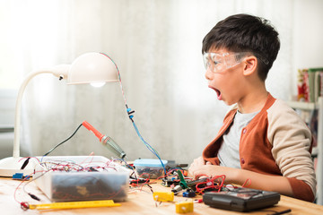 Smart looking preteen / teenage Asian boy wowing with mouth open wide successfully repairing, solid...