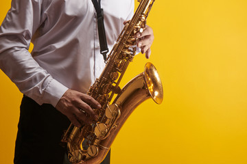 Portrait of professional musician saxophonist man in  white shirt plays jazz music on saxophone, yellow background in a photo studio, side view