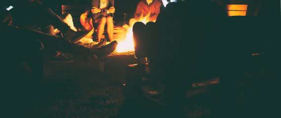 The group of friends are sitting near the bonfire in the night and talking about something