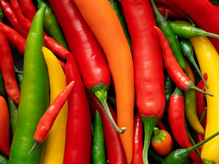 Background of mixed red, yellow, orange and green cayenne chillies from above.