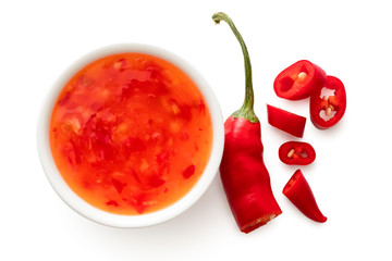 Sweet chilli sauce in a white ceramic bowl next to a cut up chilli pepper isolated on white from above.
