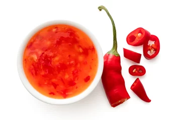Fotobehang Chili Pepers Sweet chilli sauce in a white ceramic bowl next to a cut up chilli pepper isolated on white from above.  © Moving Moment