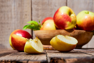 Naklejka na ściany i meble Fresh red apples with green leaves on a wooden old table. On a wooden background with sliced apple. Free space for text. soft focus