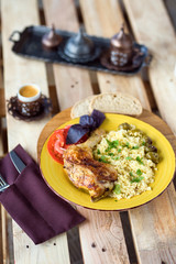 Roasted chicken leg with bulgur and herbs served with bread and coffee on a wooden background