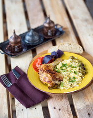 Roasted chicken leg with bulgur and herbs served with bread and coffee on a wooden background