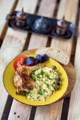 Roasted chicken leg with bulgur and herbs served with bread and coffee on a wooden background